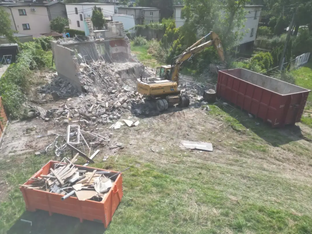 Koparka pracuje przy rozbiórce budynku. Gruz trafia do kontenerów. Oto jak zrobić opis rozbiórki.
