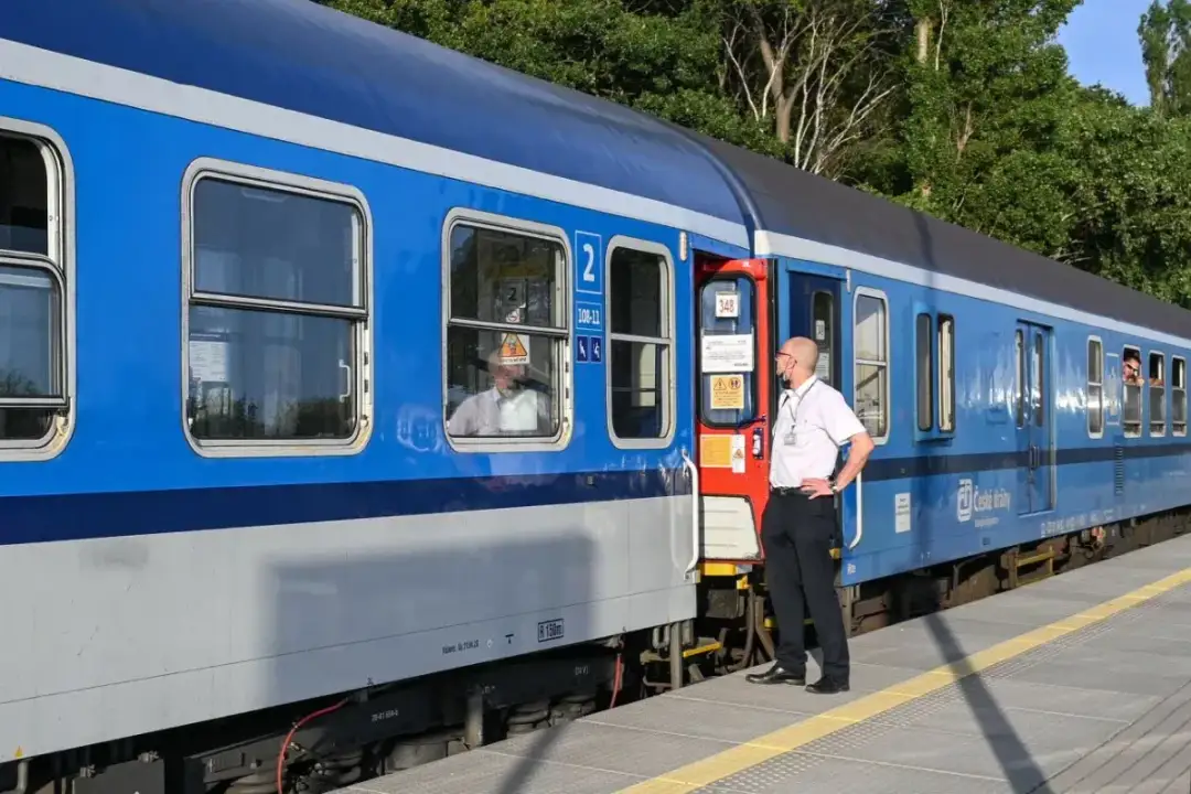 Konduktor w białej koszuli stoi przy drzwiach niebieskiego pociągu InterCity na peronie.