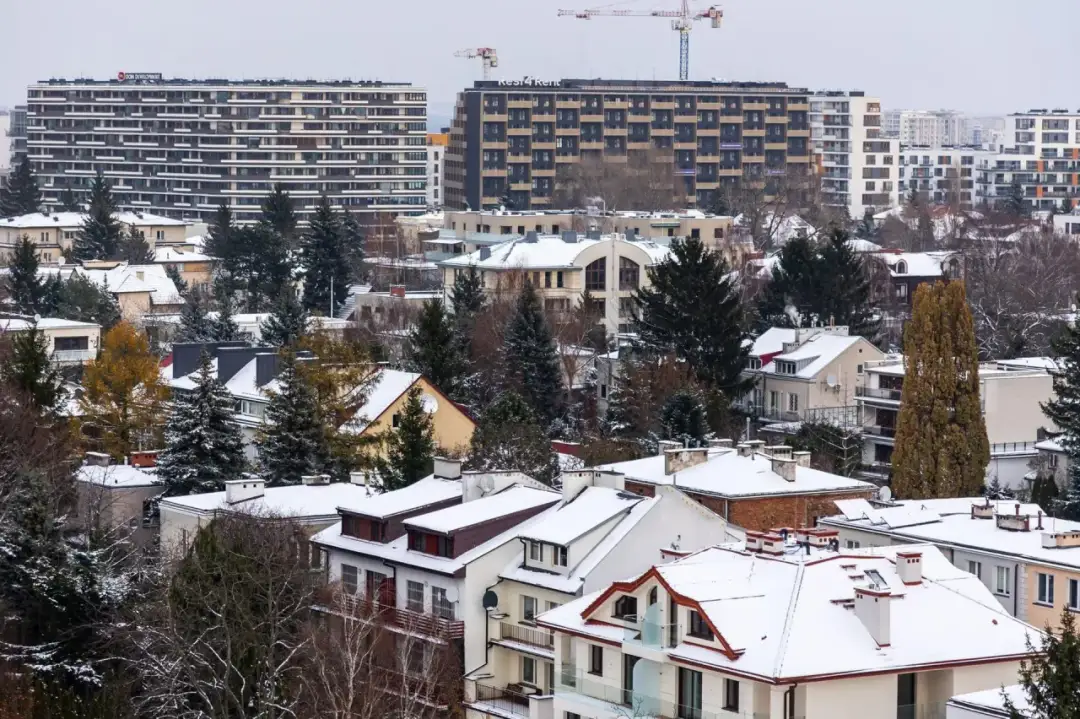 Widok na zabudowania mieszkalne pokryte śniegiem, z nowoczesnymi budynkami w tle.