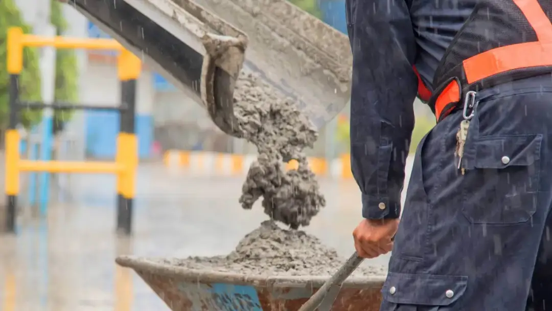 Robotnik w deszczu zasypuje taczkę betonem. Zastanawiasz się, ile kosztuje metr sześcienny betonu?