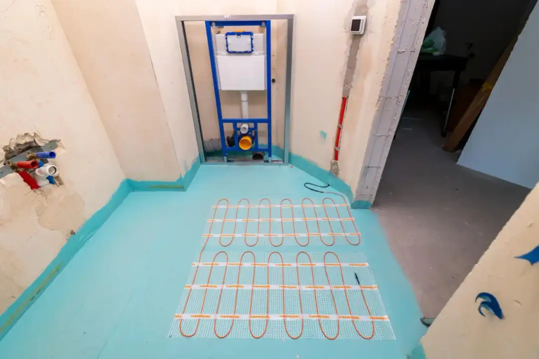 Instalacja ogrzewania podłogowego w łazience. Widać stelaż podtynkowy do WC, rury wodne i przygotowanie podłogi. To część cennika robót budowlanych.