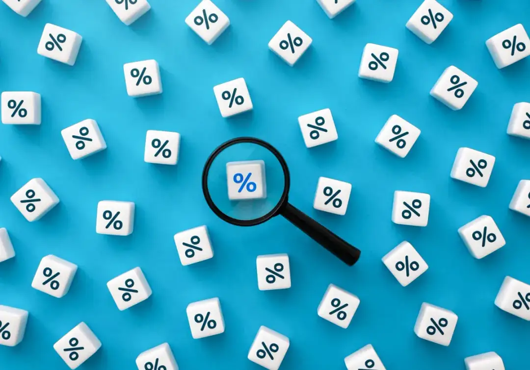 Białe kostki z symbolem procentu na niebieskim tle, jedna kostka pod lupą.