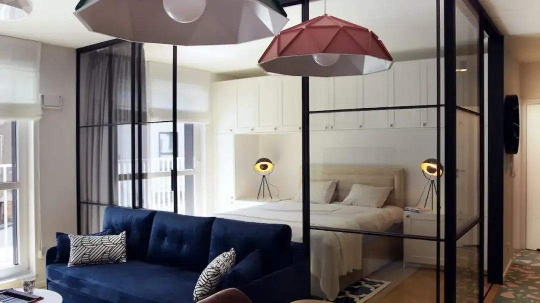 Szklana ściana z czarnymi ramami to stylowy sposób, jak oddzielić sypialnie od salonu, tworząc otwartą przestrzeń.