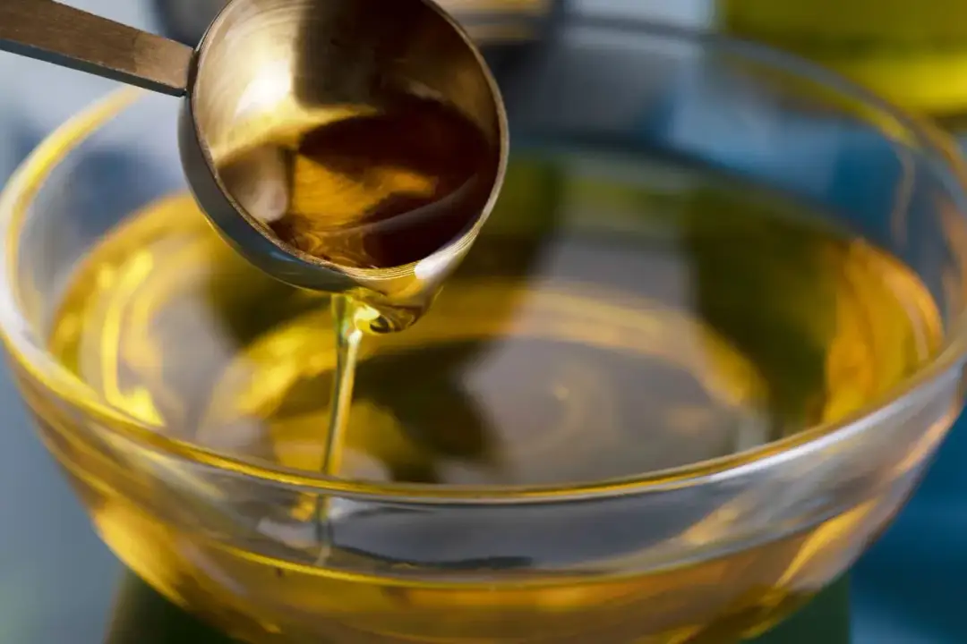 Oliwa z oliwek wylewana z miarki do szklanej miski.