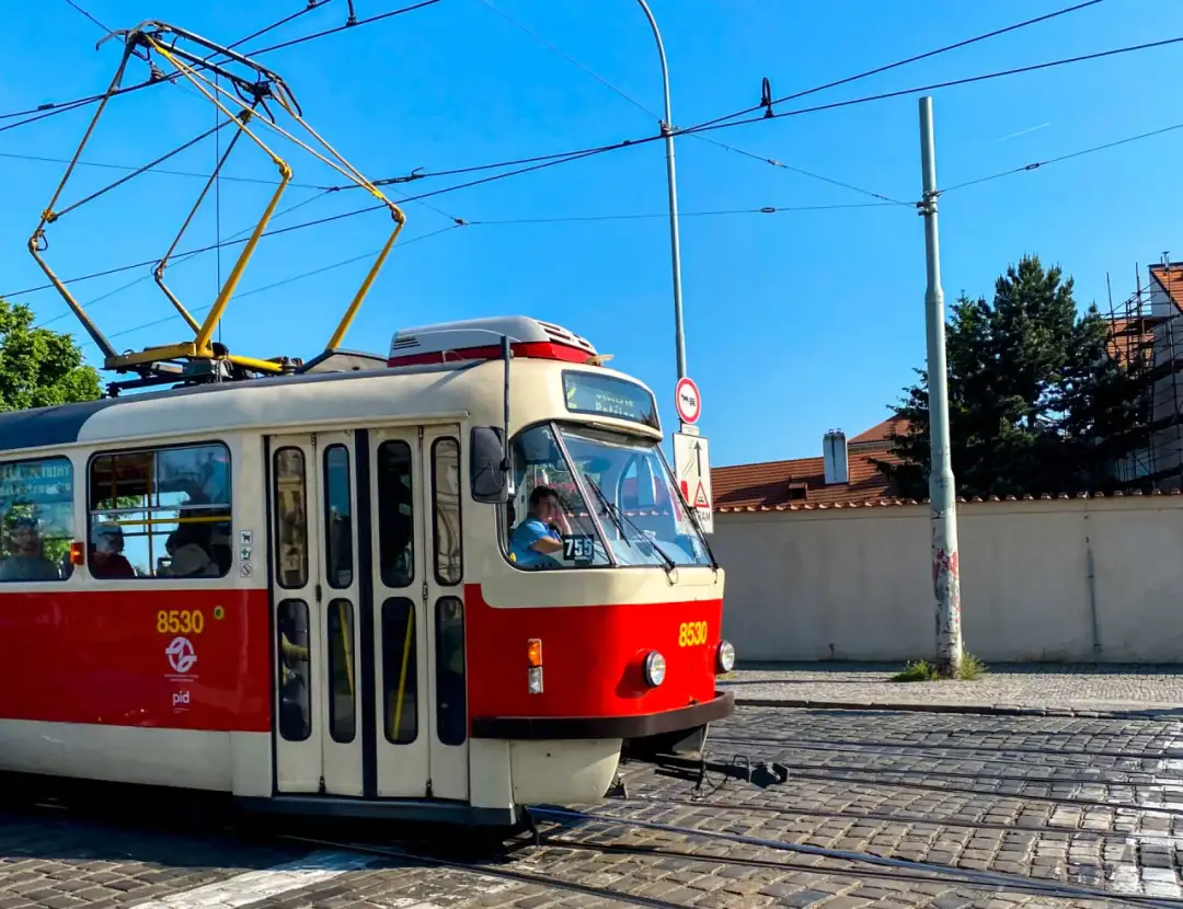 Czerwono-biały tramwaj z numerem 8530 jedzie po brukowanej ulicy. Idealny sposób, by tanio do Pragi pociągiem, a potem tramwajem po mieście.