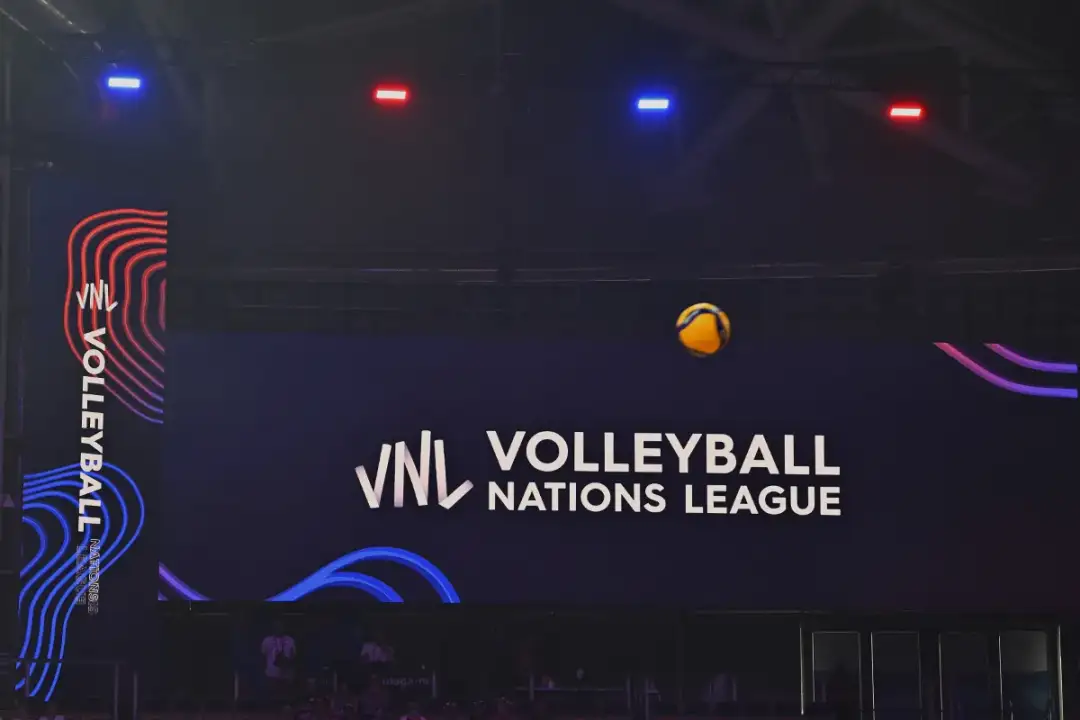 Piłka w locie nad boiskiem podczas meczu **liga narodów w siatkówce**. Na ekranie logo VNL Volleyball Nations League.
