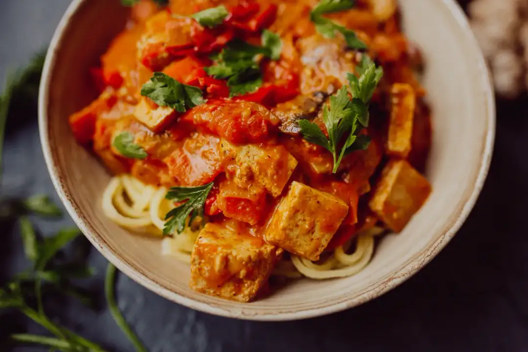 Pyszny makaron z tofu i warzywami w sosie pomidorowym, udekorowany natką pietruszki.