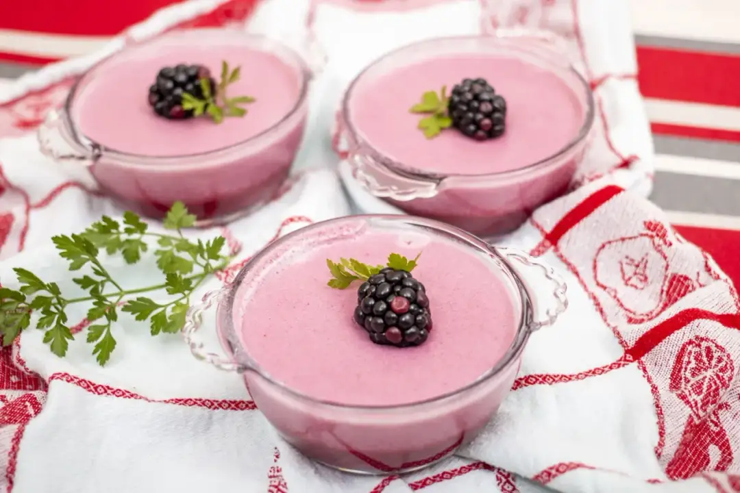 Różowa pianka z galaretki, udekorowana jeżyną i natką pietruszki, w szklanych pucharkach. Idealna na deser, łatwa do zrobienia.