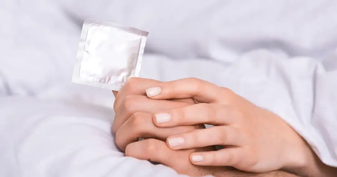 Dłonie trzymają prezerwatywę. Czy wytrysk w prezerwatywie jest bezpieczny? Tak, przy prawidłowym użyciu.