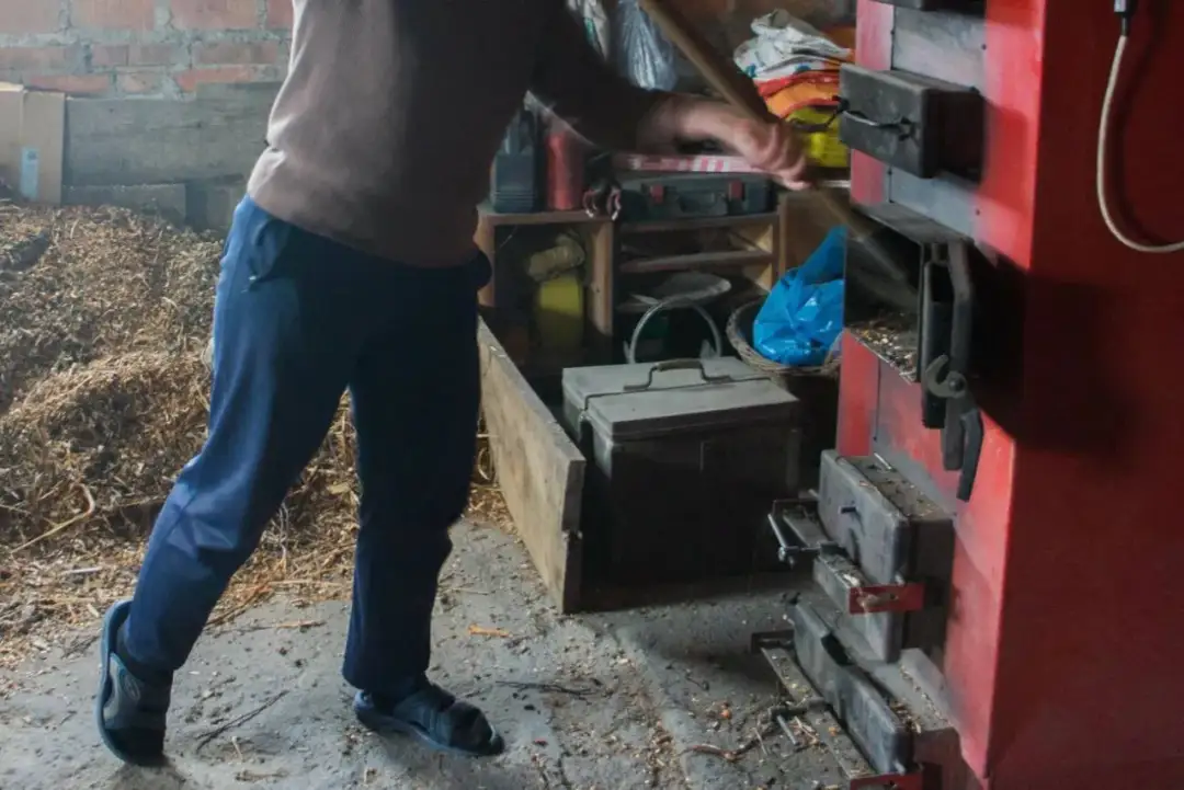 Osoba wsypuje materiał do czerwonego pieca na pellet.