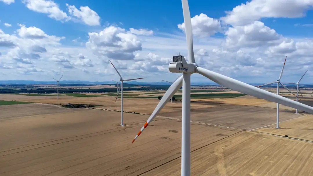 Widok z lotu ptaka na farmę wiatrową na tle błękitnego nieba z chmurami.
