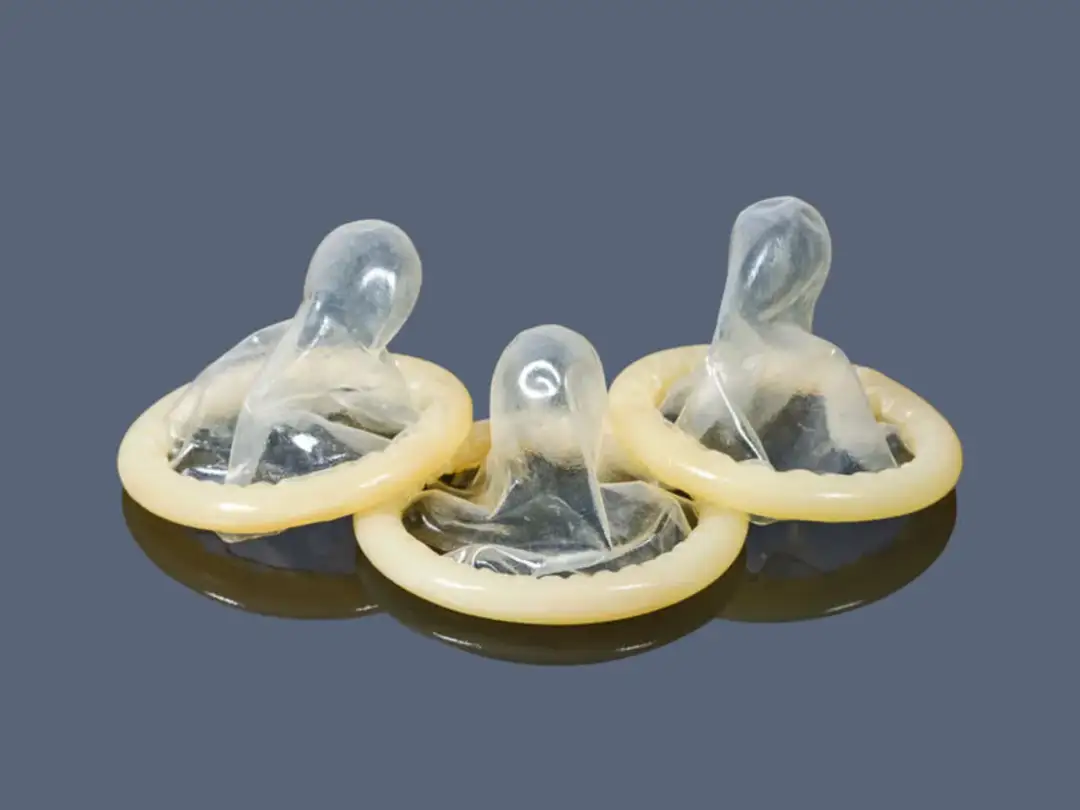 Trzy prezerwatywy bez lateksu, przezroczyste, z żółtym pierścieniem, na ciemnym tle.