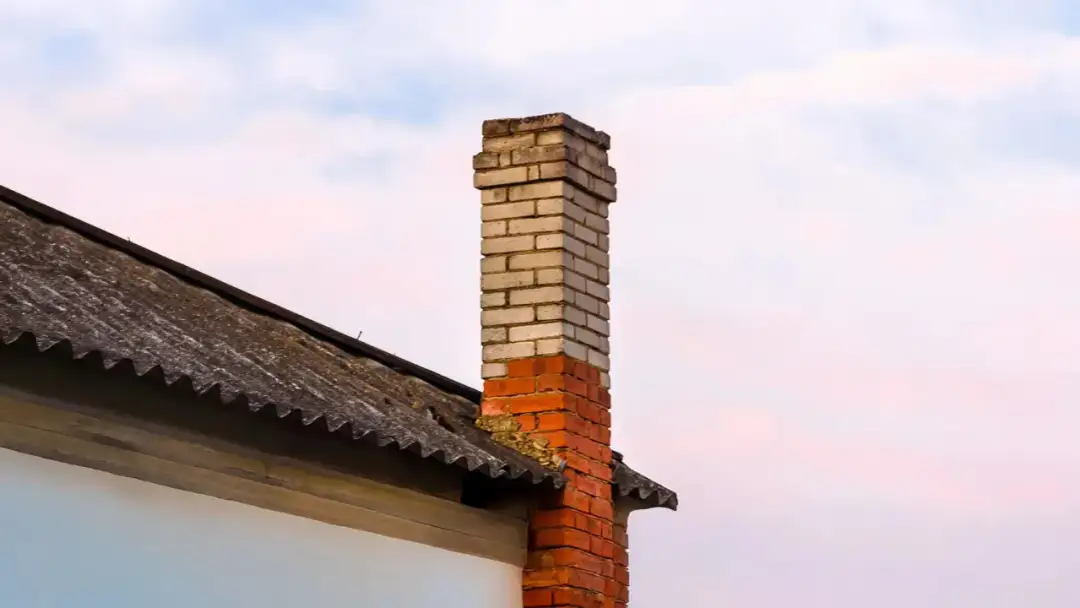 Ceglany komin na dachu z eternitu, na tle nieba.