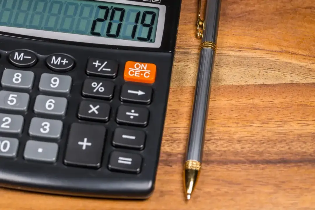 Kalkulator z wyświetlaczem 2019 i długopis na drewnianym tle.