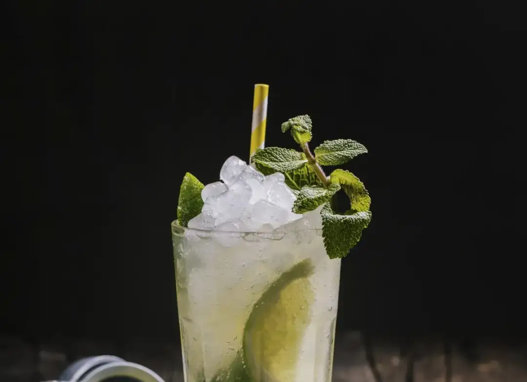 Orzeźwiający mojito drink ze spritem, lodem, limonką i miętą, z żółto-białą słomką.