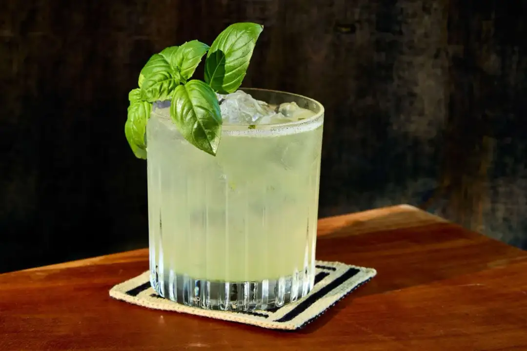 Orzeźwiający gin basil smash z listkami bazylii, podany na lodzie w szklance na drewnianym blacie.