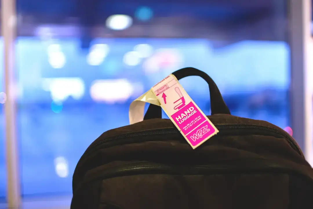 Różowa etykieta "HAND LUGGAGE" Wizz Air na czarnym plecaku.