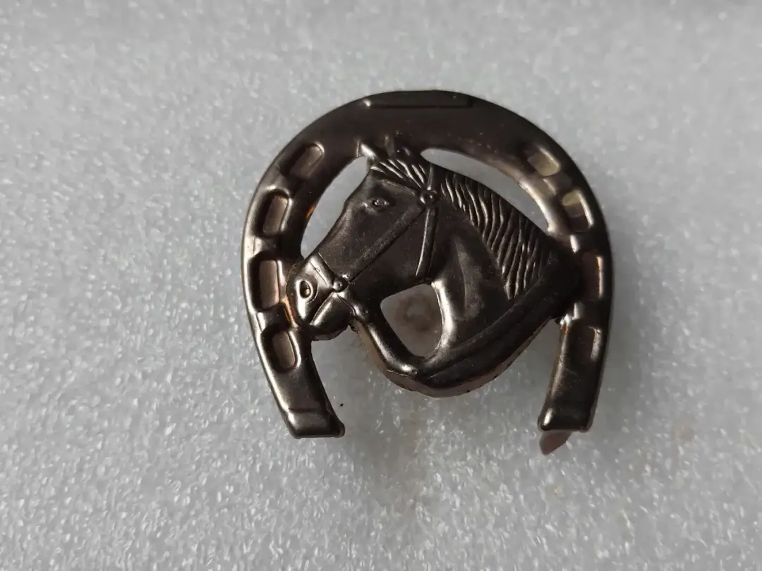 Metalowa odznaka w kształcie podkowy z głową konia.