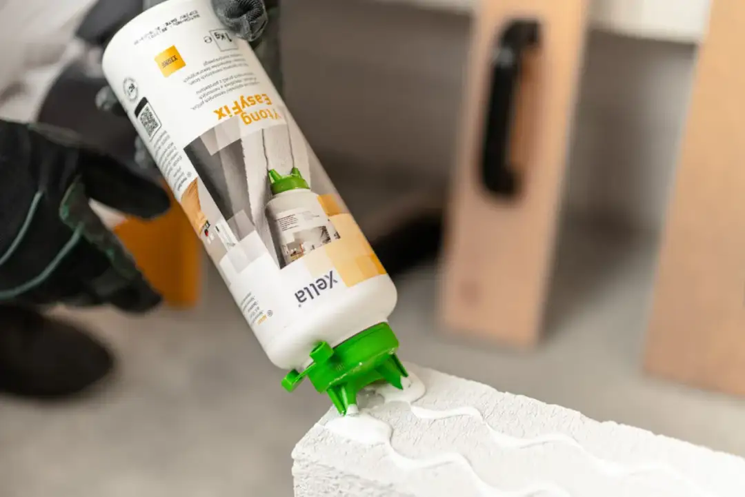 Ręce w rękawicach aplikują klej Ytong EasyFix na bloczek. Czy klejem do płytek można murować? Ten klej jest do bloczków Ytong.