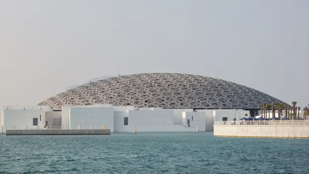 Imponująca kopuła Luwru Abu Zabi, z geometrycznym wzorem, góruje nad białymi budynkami i turkusową wodą.