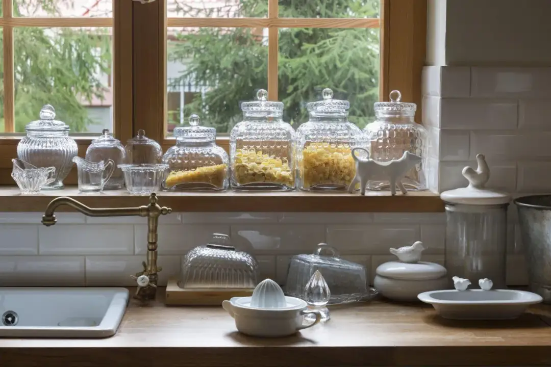 Szklane słoje z makaronem i ozdobne figurki zwierząt na parapecie w kuchni.