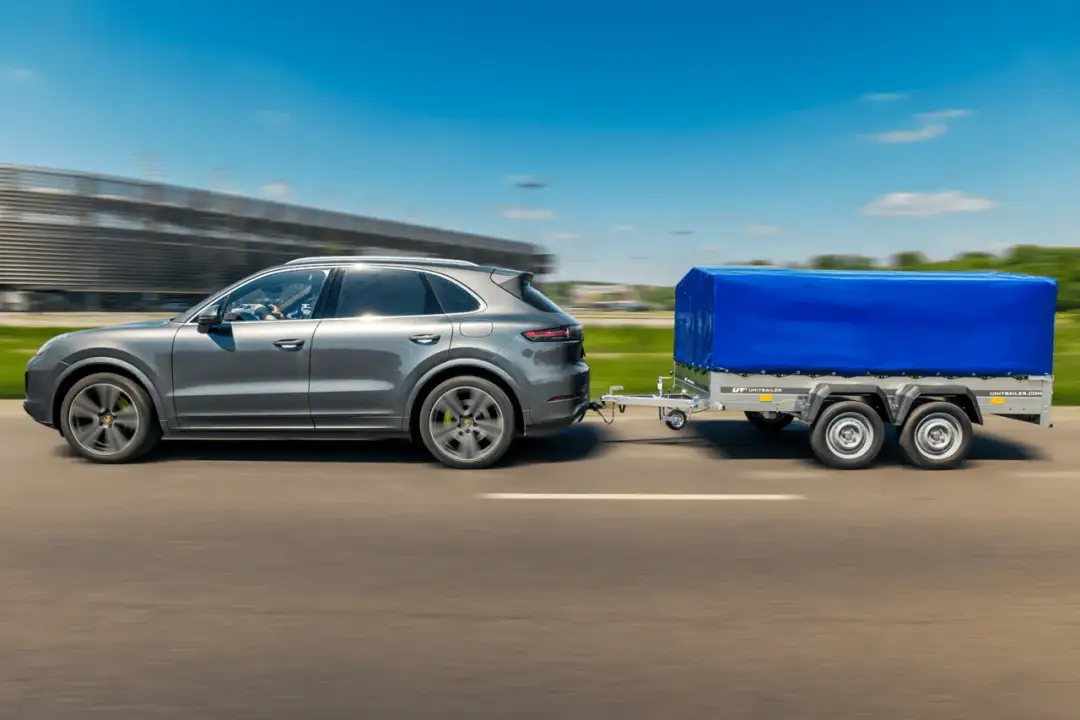 Szary SUV ciągnie przyczepę kempingową pod niebieską plandeką. Zastanawiasz się, ile kosztuje przerejestrowanie przyczepy kempingowej?