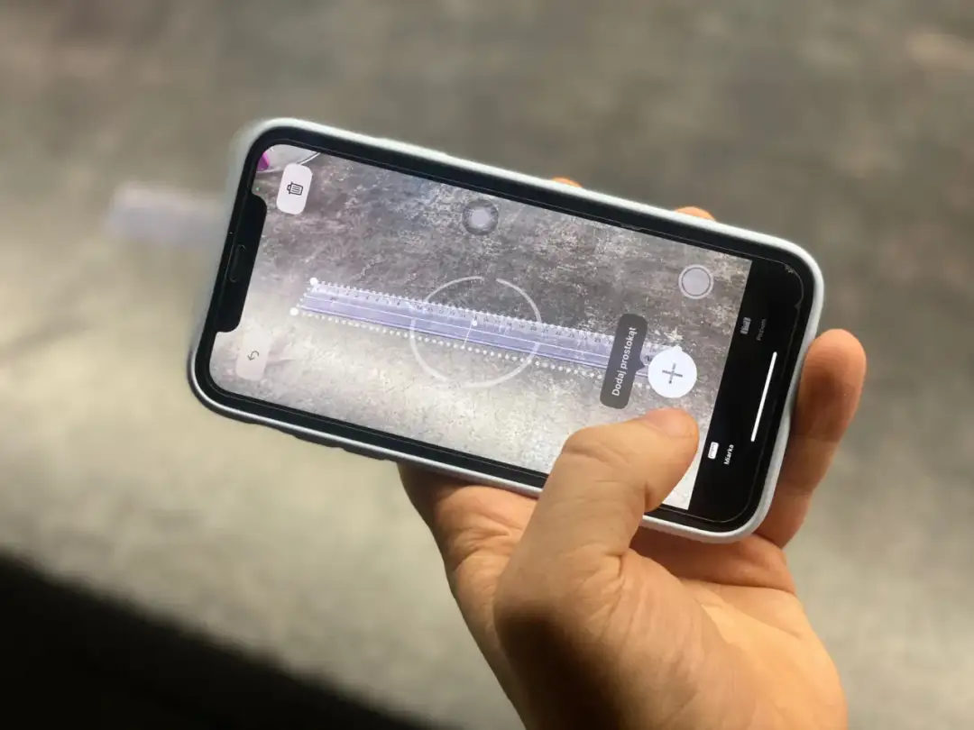 Dłoń trzyma telefon, na ekranie którego widać wirtualną miarkę cm.