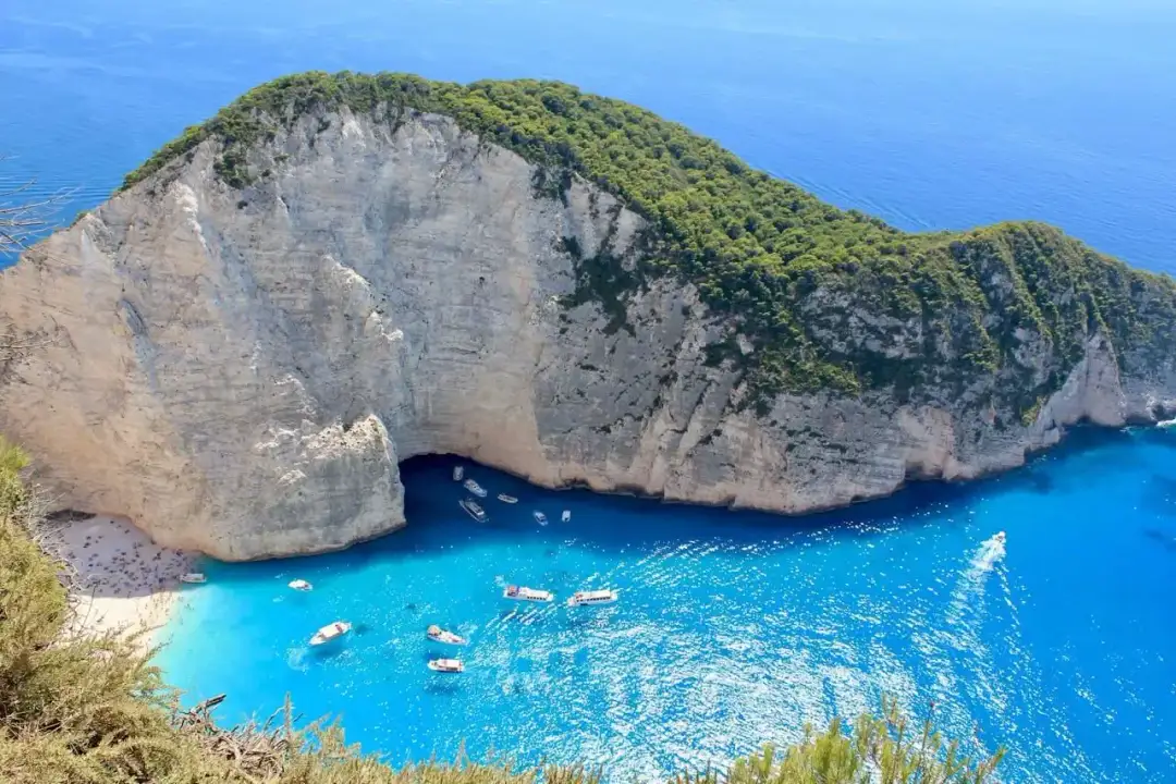 Widok na zatokę Navagio na Zakynthos z białymi klifami, turkusową wodą i łodziami.