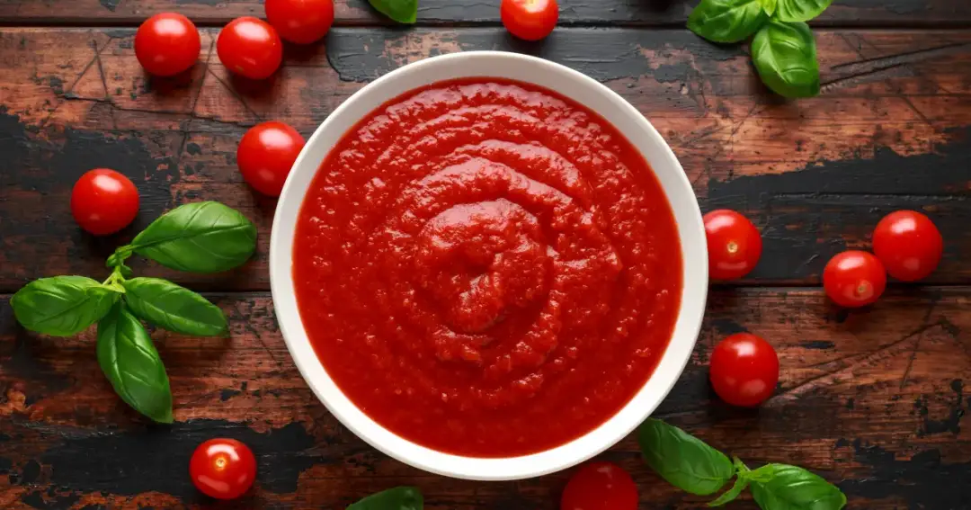 Miseczka pełna pomidorowej passaty, otoczona świeżymi pomidorkami i bazylią. Czy passata pomidorowa jest lekkostrawna? Tak, zazwyczaj tak.