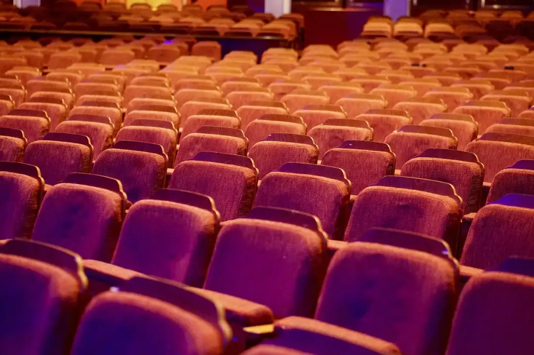 Puste, czerwone fotele teatralne w rzędach, oświetlone ciepłym światłem.