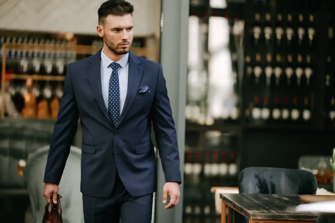 Elegancki mężczyzna w granatowym garniturze, idealny przykład, jak się ubrać do teatru na komedię. W dłoni trzyma brązową teczkę.