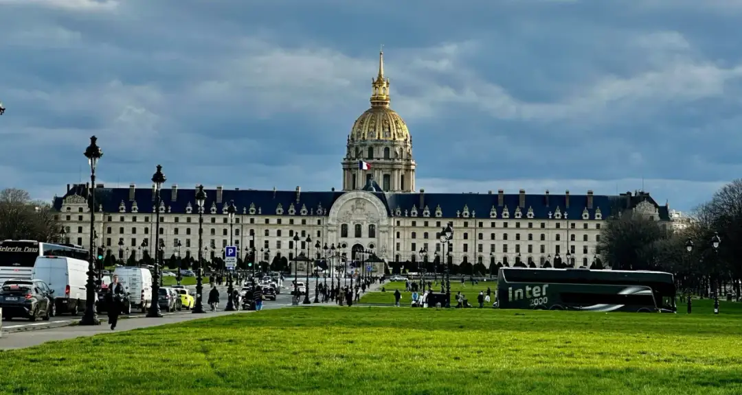 Złota kopuła Les Invalides góruje nad placem w Paryżu. Ruch uliczny i zielony trawnik tworzą tło dla tego historycznego miejsca.