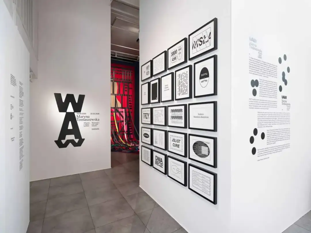 Wystawa w muzeum sztuki nowoczesnej prezentuje prace Maryny Tomaszewskiej. Na ścianie widnieje logo WA oraz grafiki z datami i tytułami.