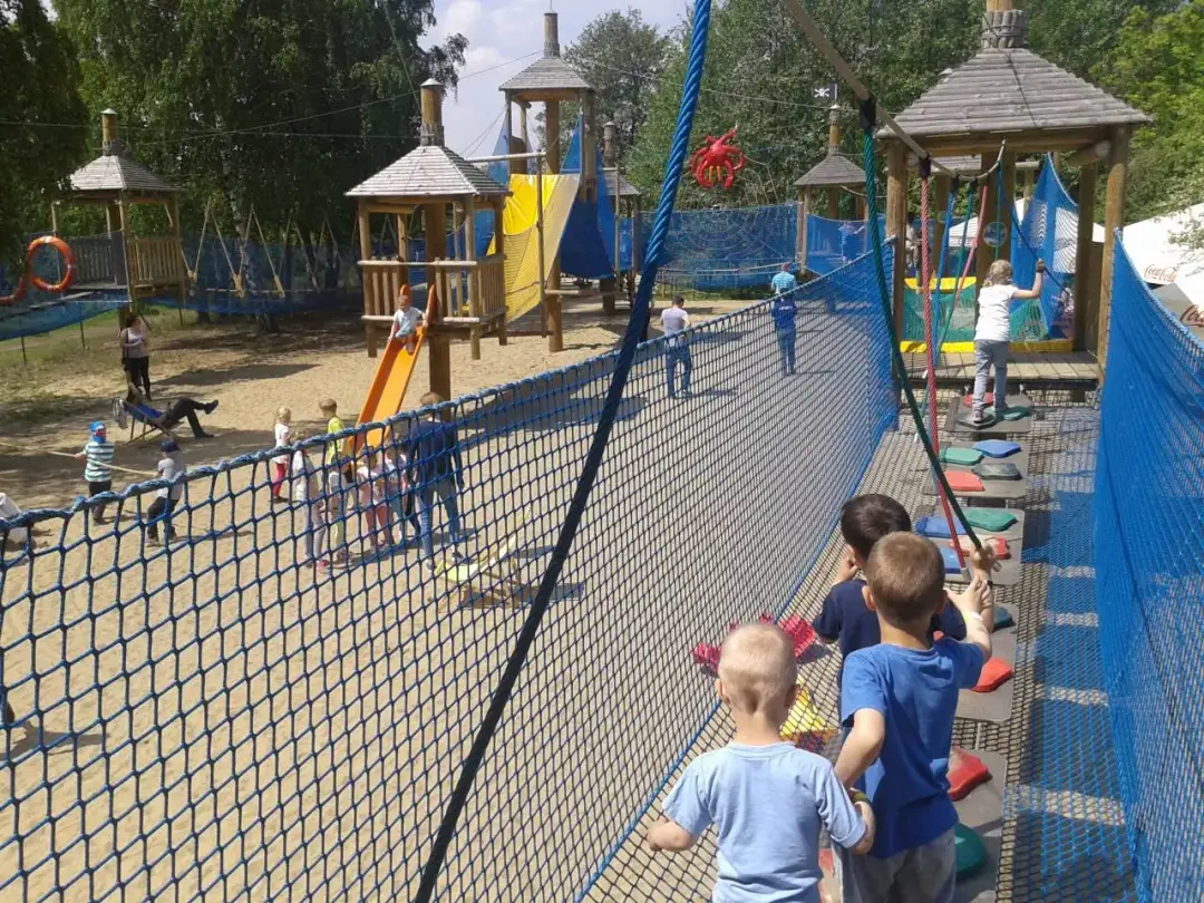 Dzieci bawią się na placu zabaw w parku linowym, pokonując przeszkody.