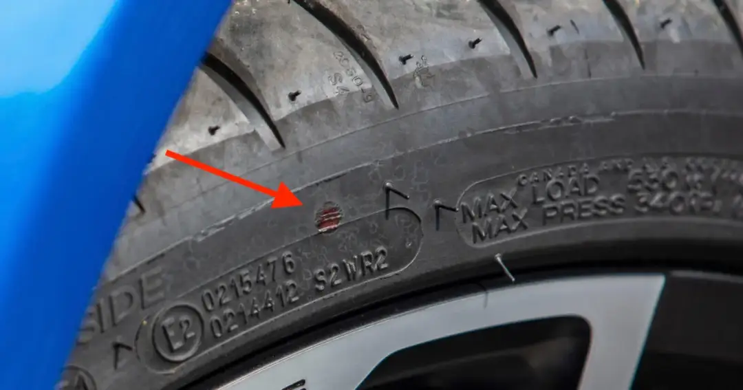 Czerwona strzałka wskazuje na uszkodzenie opony. Kropki na oponach mogą oznaczać różne rzeczy, np. punkty kontrolne jakości.