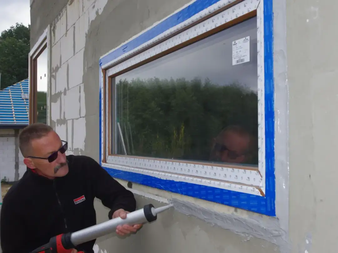 Mężczyzna z pistoletem na masę uszczelniającą zabezpiecza piankę przy nowym oknie.