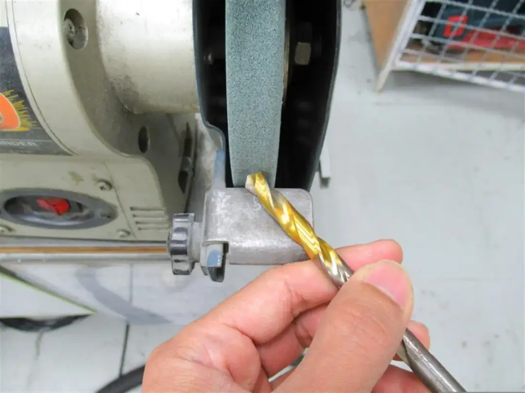 Dłoń trzyma wiertło do metalu przy ostrzałce.