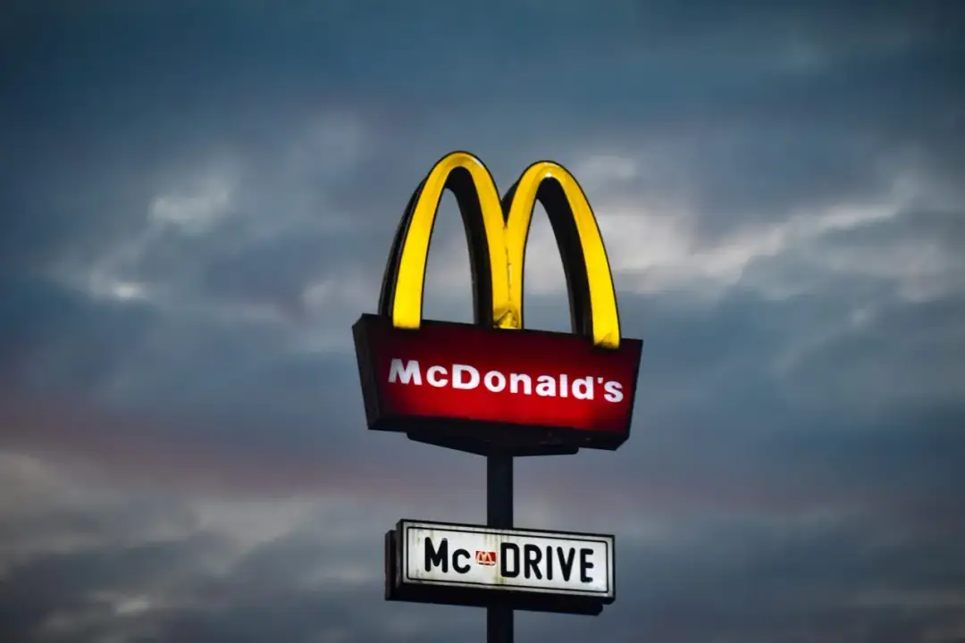 Podświetlany znak McDonald's z napisem "McDRIVE" na tle zachmurzonego nieba.