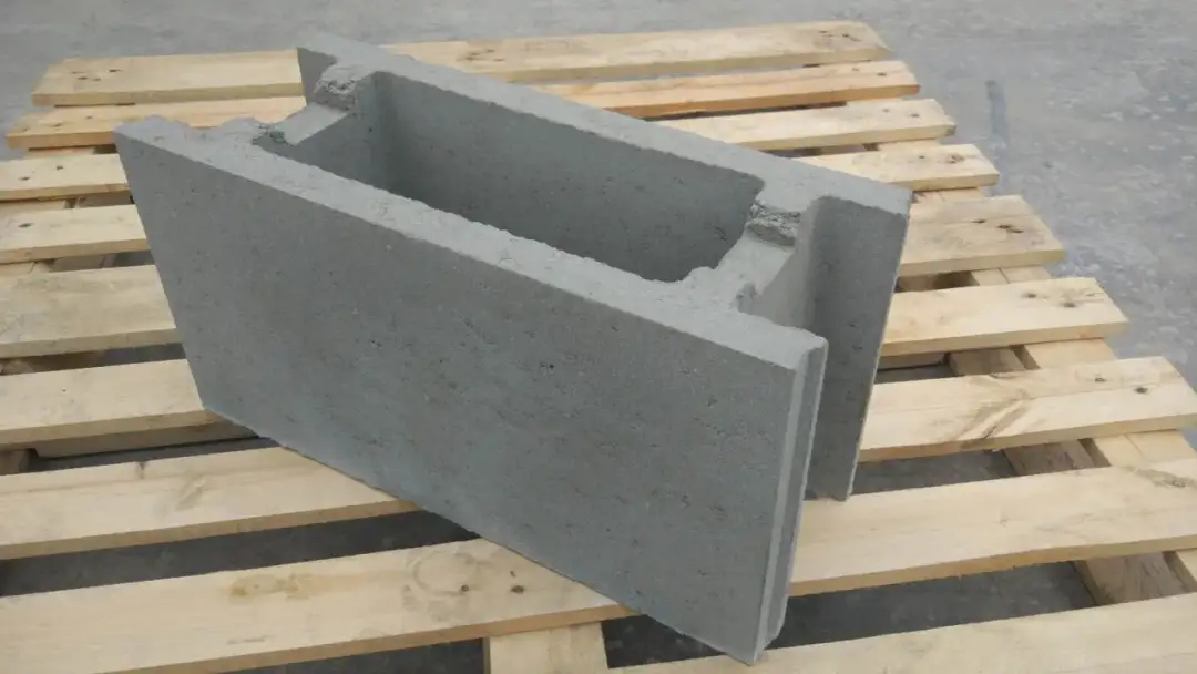 Szary pustak zalewowy na drewnianej palecie. Zastanawiasz się, ile betonu do pustaka zalewowego? Ten pustak ma puste wnętrze, gotowe do wypełnienia.