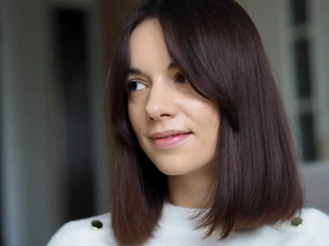 Kobieta z brązowymi włosami i naturalnym makijażem, uśmiecha się lekko.