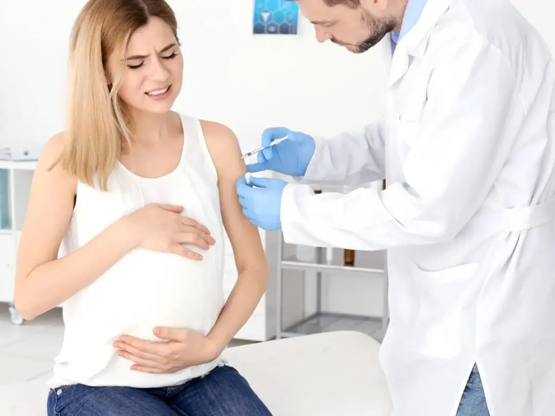 Lekarz podaje szczepionkę w ramię ciężarnej kobiety, która odczuwa ból. To ważna profilaktyka, by chronić ją i dziecko przed chorobami, np. jelitówką.