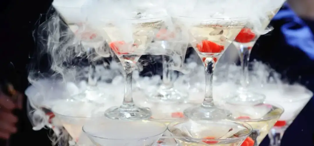 Efektowne drinki z suchym lodem tworzą mglistą, tajemniczą atmosferę. Kieliszki wypełnione są złotym płynem i ozdobione czerwonymi owocami.