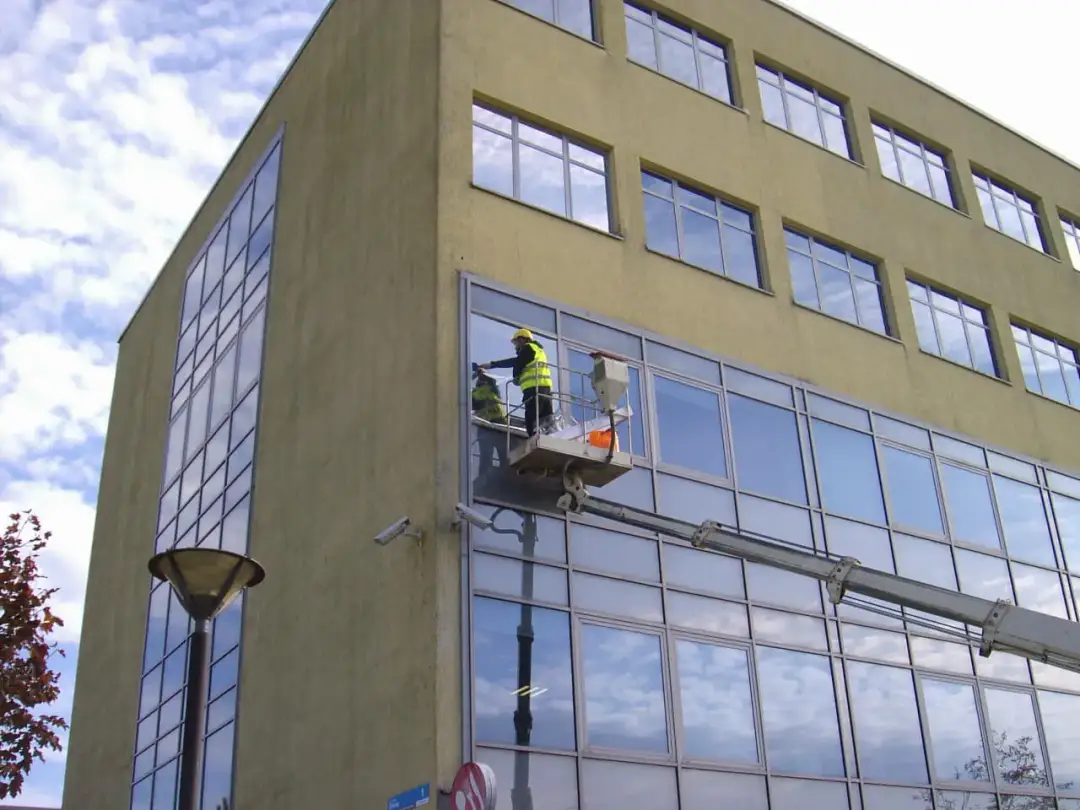 Pracownicy na podnośniku montują okno w nowoczesnym budynku.