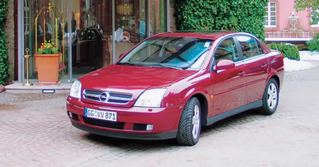Czerwony Opel Vectra C GTS zaparkowany przed wejściem do hotelu.