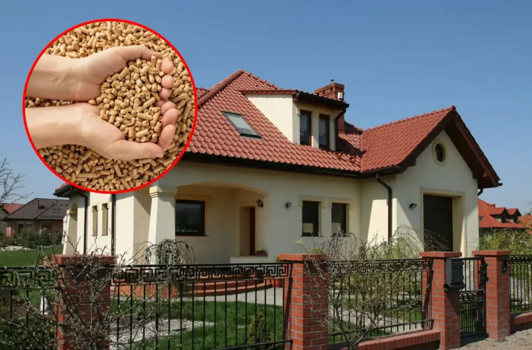 Dłonie trzymające pellet na tle domu z czerwonym dachem.