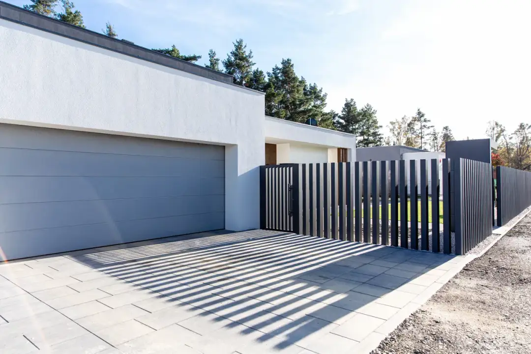 Nowoczesny podjazd bez ogrodzenia, z szarą bramą garażową i pionowym płotem.