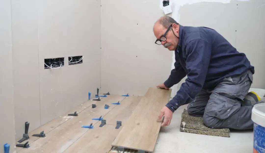 Mężczyzna w okularach układa panele podłogowe, używając klipsów dystansowych.