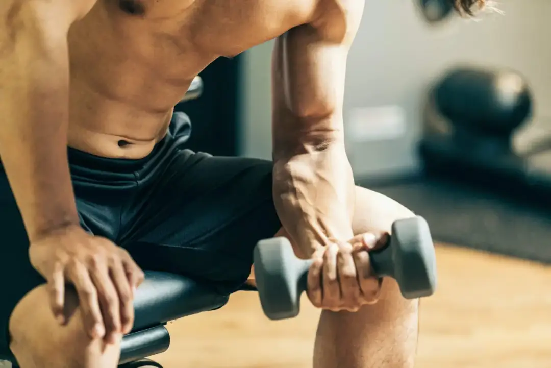 Mężczyzna ćwiczy biceps z hantlem, zastanawiając się, czy można ćwiczyć codziennie.