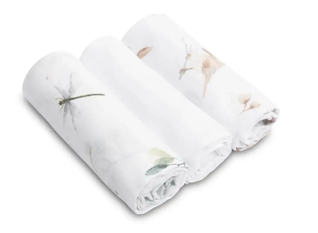 Trzy białe pieluchy muślinowe z delikatnymi wzorami: ważka, ptaszek i liście.