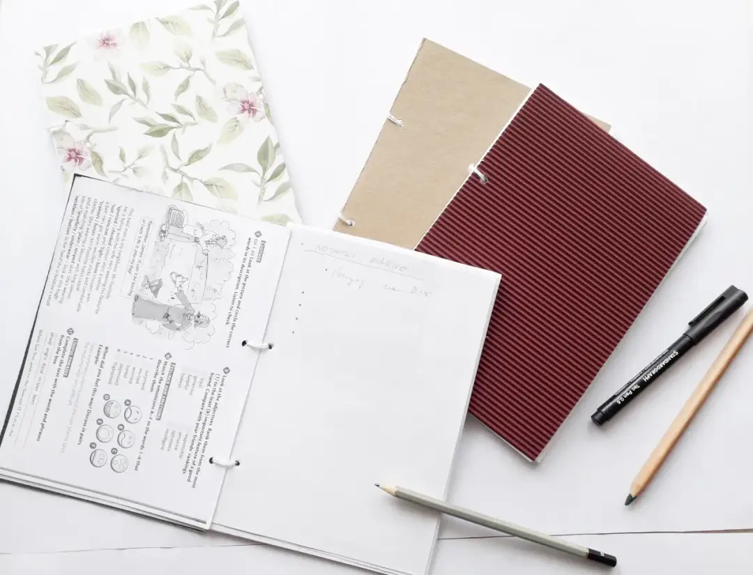 Notatniki z kartek, ołówki i długopis na białym tle.